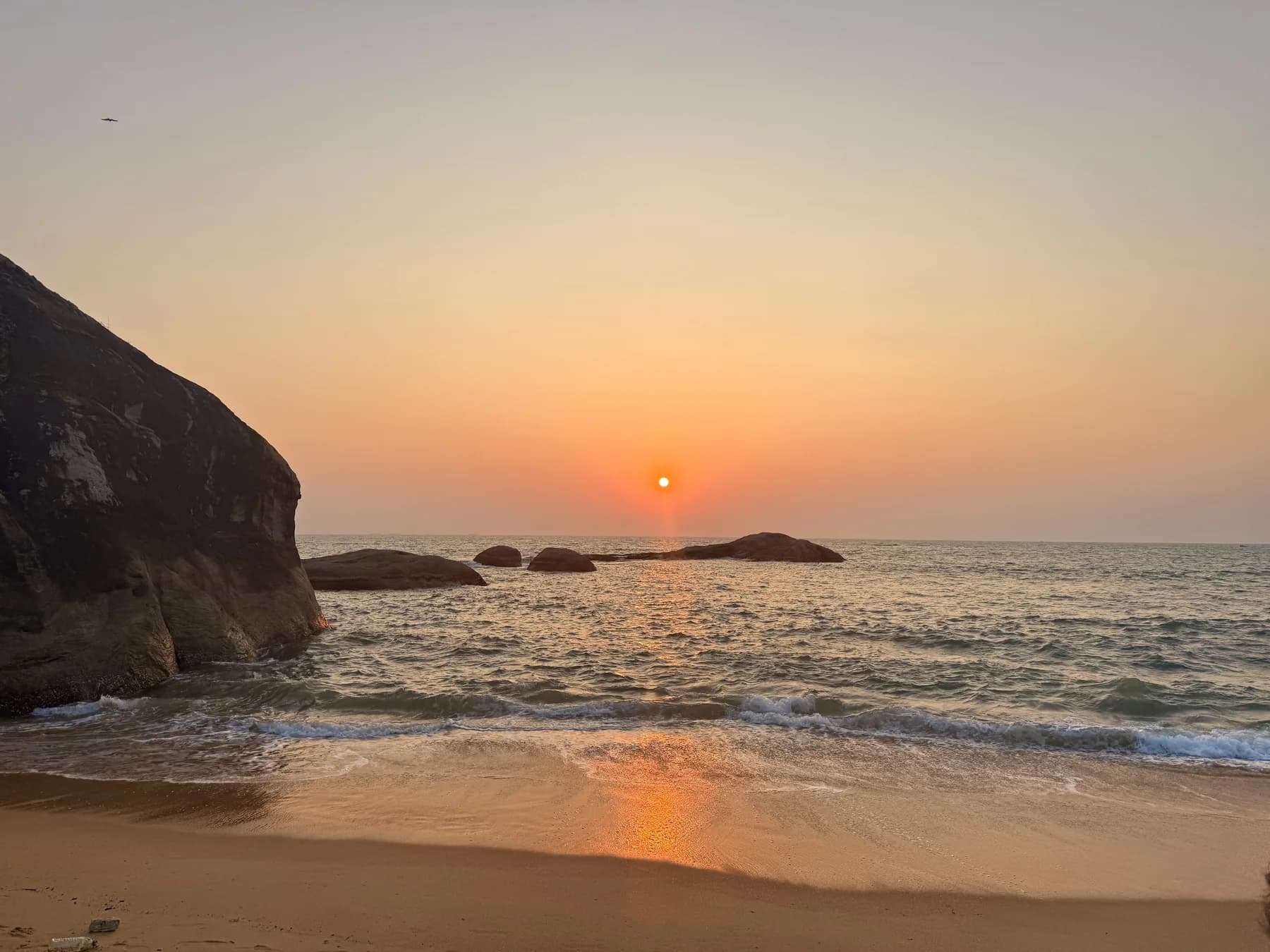 The sun setting over the sea between rocks on a sandy beach